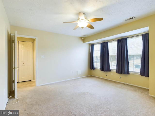 empty room featuring light colored carpet, visible vents, a textured ceiling, and baseboards