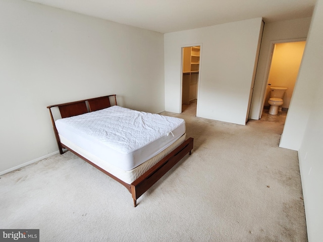 bedroom with a walk in closet, connected bathroom, light colored carpet, and a closet