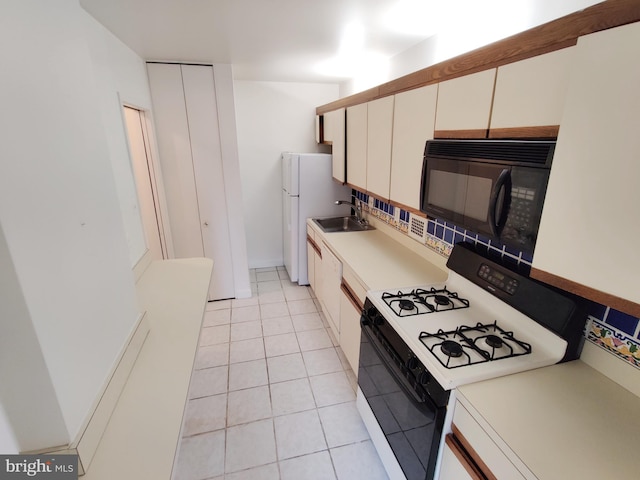 kitchen with light tile patterned floors, sink, tasteful backsplash, white cabinets, and range with gas cooktop