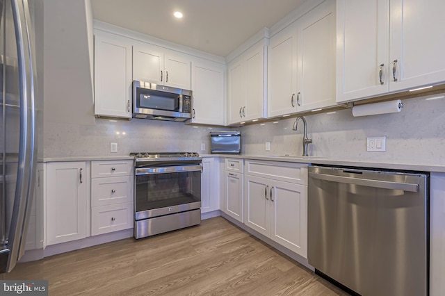 kitchen with decorative backsplash, appliances with stainless steel finishes, light wood-type flooring, sink, and white cabinetry