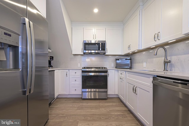 kitchen featuring backsplash, sink, appliances with stainless steel finishes, white cabinetry, and wood-type flooring