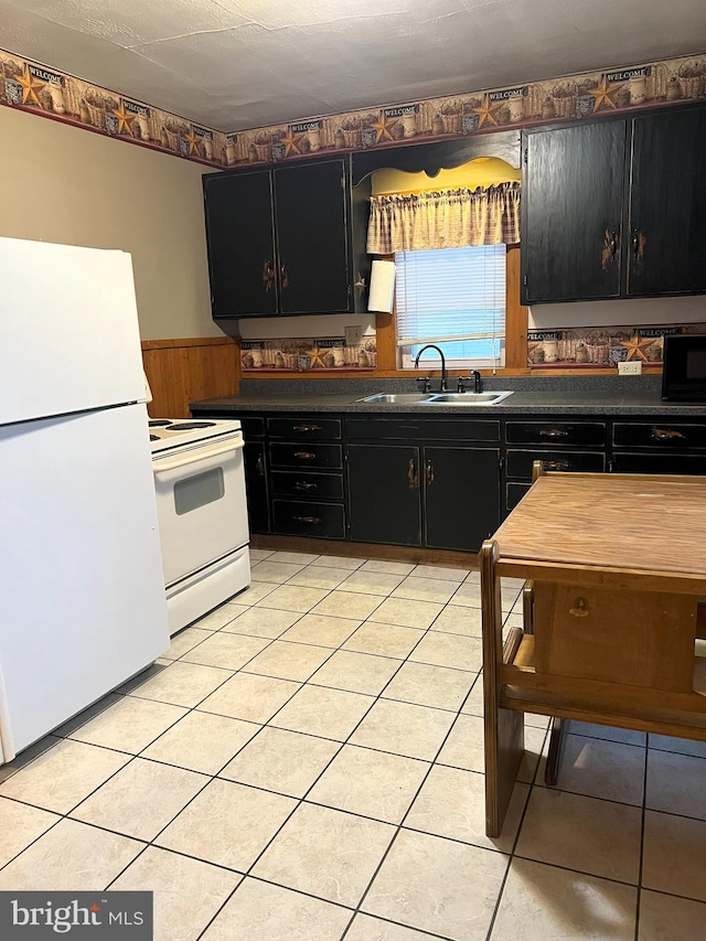 kitchen featuring wood walls, light tile patterned flooring, white appliances, and sink