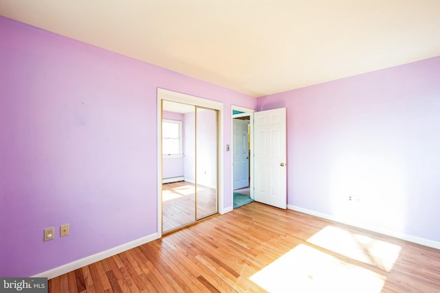 unfurnished bedroom featuring a baseboard heating unit, a closet, and light hardwood / wood-style flooring