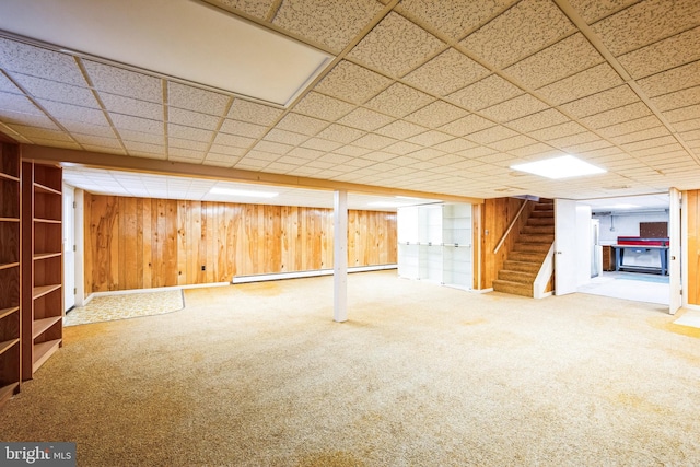 basement with a paneled ceiling, wooden walls, carpet flooring, and a baseboard heating unit