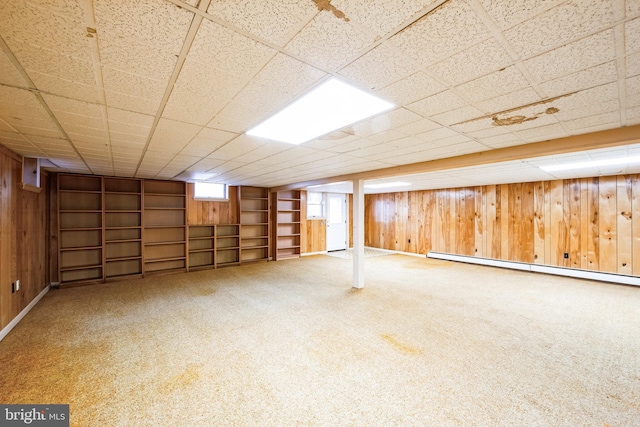 basement featuring a drop ceiling, carpet flooring, baseboard heating, and wooden walls