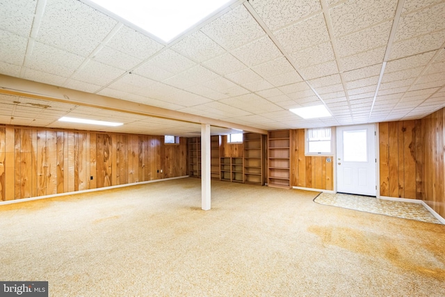 basement with carpet floors, wood walls, and a paneled ceiling