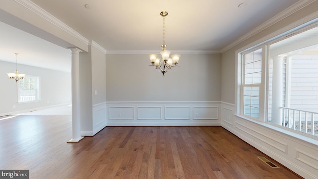 empty room with a chandelier, hardwood / wood-style floors, ornate columns, and crown molding