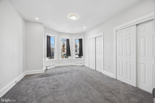 unfurnished bedroom featuring carpet flooring, two closets, and a baseboard heating unit