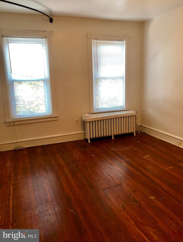 unfurnished room featuring radiator, plenty of natural light, and dark wood-type flooring