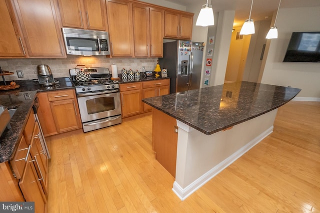 kitchen with appliances with stainless steel finishes, backsplash, dark stone counters, pendant lighting, and a kitchen island