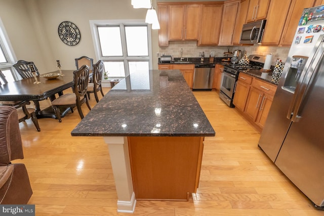 kitchen with backsplash, sink, light hardwood / wood-style flooring, a kitchen island, and stainless steel appliances