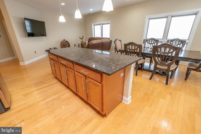 kitchen with light wood-type flooring, pendant lighting, a center island, and dark stone countertops