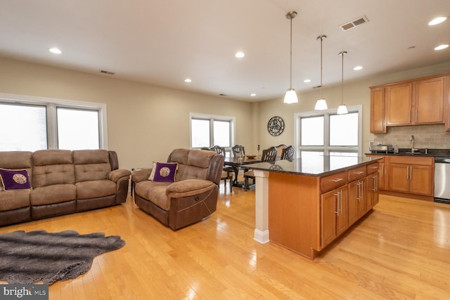 kitchen featuring stainless steel dishwasher, sink, pendant lighting, light hardwood / wood-style flooring, and a kitchen island