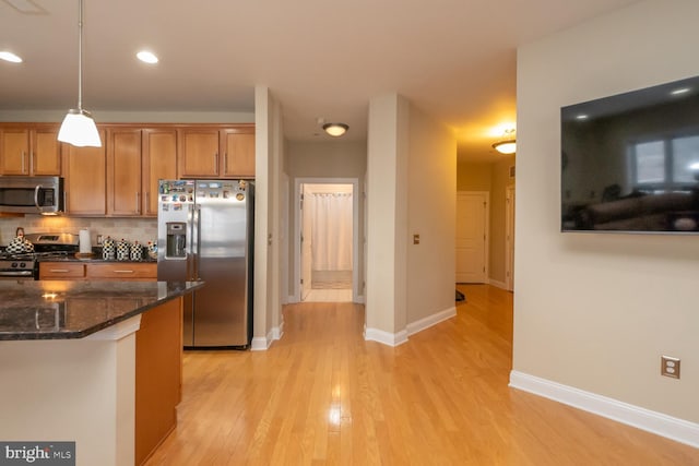 kitchen featuring decorative backsplash, dark stone counters, stainless steel appliances, pendant lighting, and light hardwood / wood-style floors