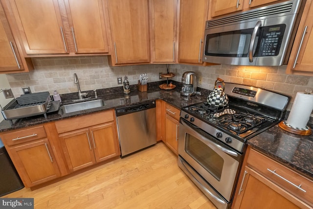 kitchen featuring dark stone counters, sink, stainless steel appliances, and light hardwood / wood-style floors