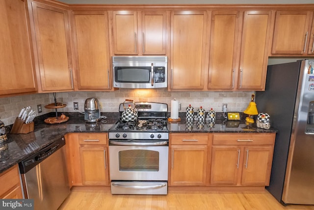 kitchen featuring dark stone counters, light hardwood / wood-style flooring, appliances with stainless steel finishes, and tasteful backsplash