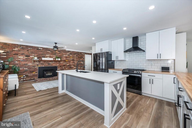 kitchen featuring wall chimney exhaust hood, stainless steel range, white cabinetry, black fridge with ice dispenser, and butcher block counters