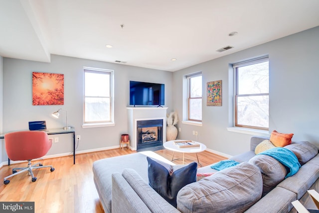 living room with plenty of natural light, visible vents, wood finished floors, and a glass covered fireplace