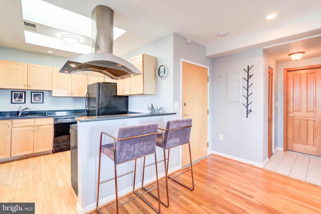 kitchen featuring light wood finished floors, dark countertops, light brown cabinets, a sink, and black appliances