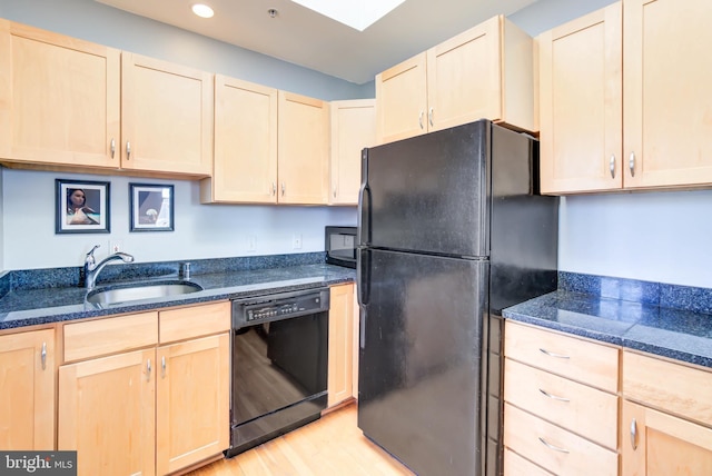 kitchen featuring light wood-style flooring, light brown cabinets, a sink, dark stone countertops, and black appliances