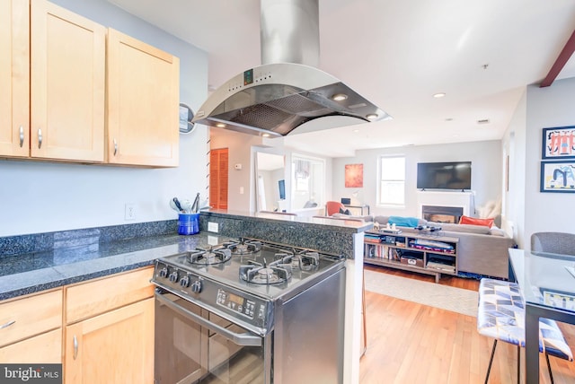 kitchen with light brown cabinets, a peninsula, light wood-type flooring, stainless steel gas stove, and island exhaust hood