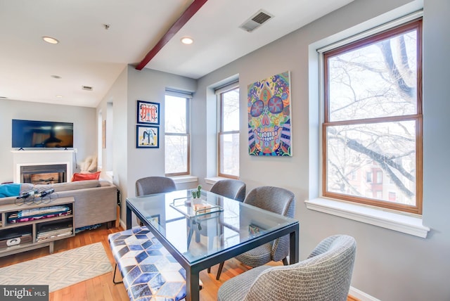 dining room featuring baseboards, visible vents, a glass covered fireplace, wood finished floors, and recessed lighting