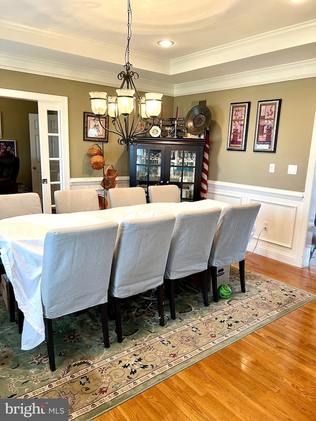 dining area with wood-type flooring, a tray ceiling, crown molding, and a notable chandelier