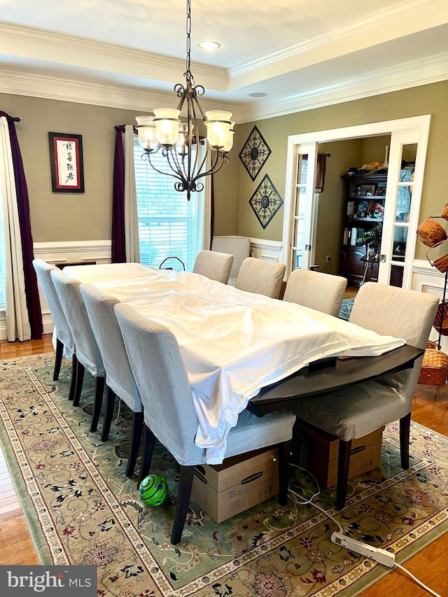 dining area featuring a raised ceiling, a notable chandelier, wood-type flooring, and ornamental molding