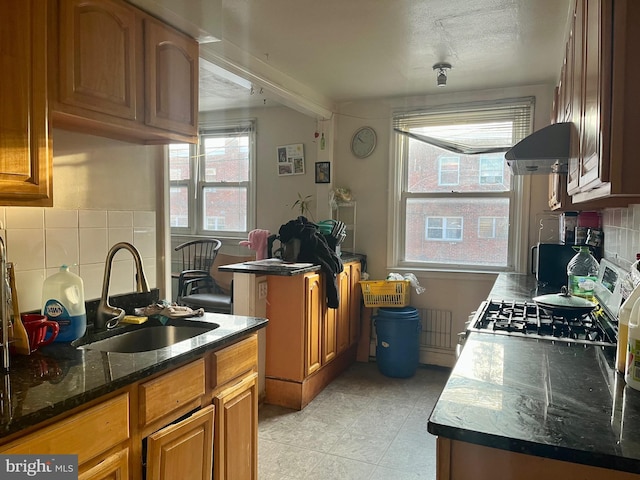 kitchen with sink, a center island, backsplash, dark stone countertops, and stove