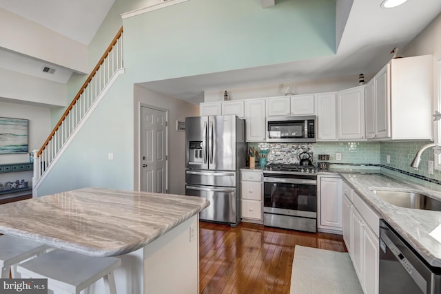 kitchen with white cabinets, stainless steel appliances, a center island, light stone countertops, and sink