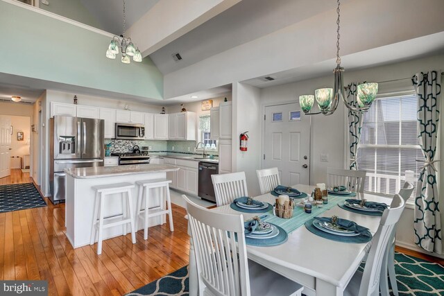 dining room featuring light wood-type flooring, plenty of natural light, high vaulted ceiling, and a chandelier