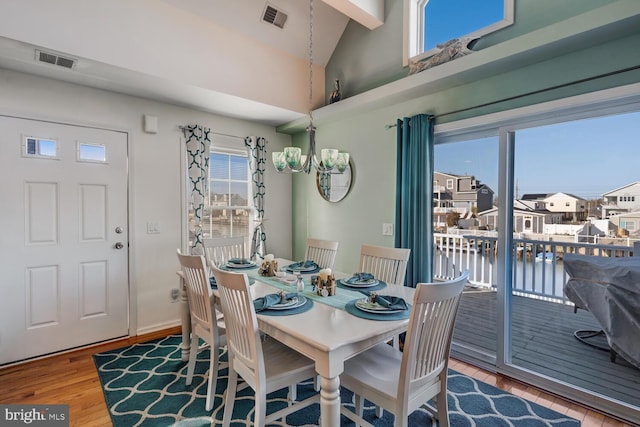 dining space featuring a water view, an inviting chandelier, lofted ceiling, and wood-type flooring