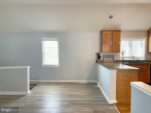 kitchen with kitchen peninsula, sink, pendant lighting, and wood-type flooring