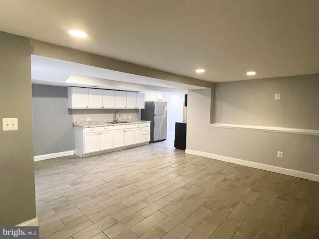 kitchen featuring stainless steel fridge, light wood-type flooring, light stone counters, sink, and white cabinetry