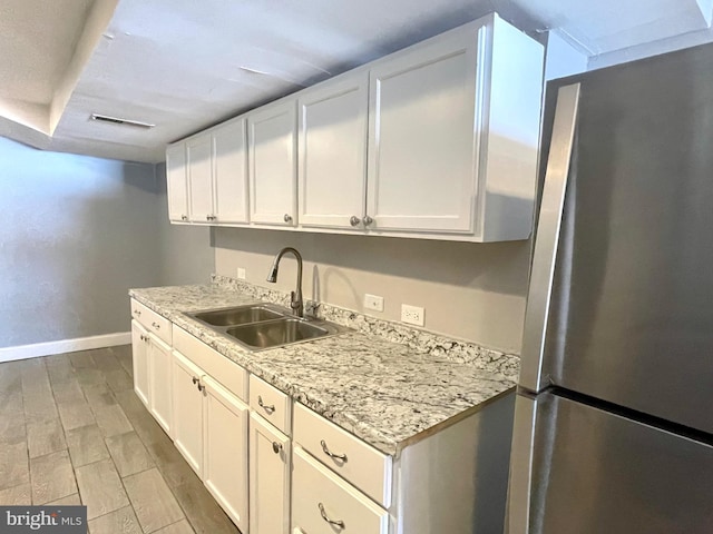 kitchen with white cabinets, stainless steel fridge, light stone countertops, and sink