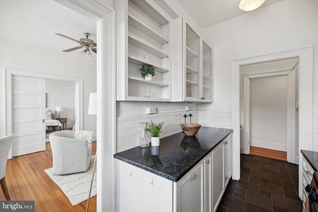 kitchen featuring decorative backsplash, ceiling fan, dark stone countertops, and white cabinetry