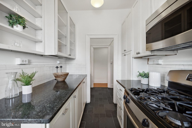 kitchen with white cabinets, appliances with stainless steel finishes, decorative backsplash, and dark stone counters