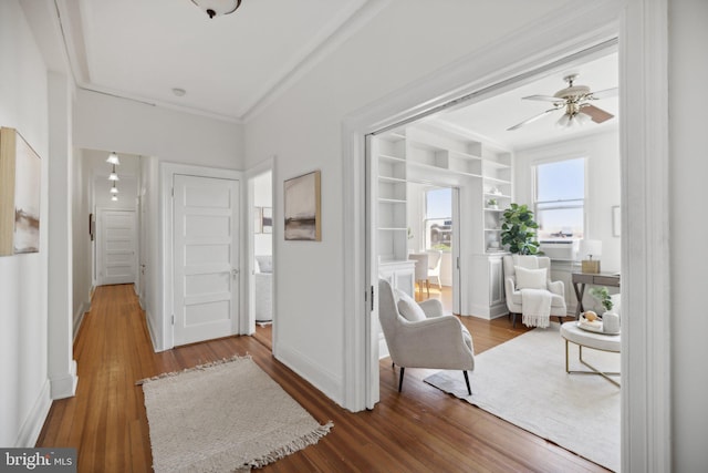 sitting room featuring built in shelves, ceiling fan, wood-type flooring, and crown molding