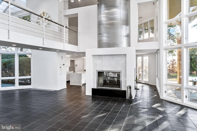 unfurnished living room featuring a high end fireplace, dark tile patterned floors, and a high ceiling