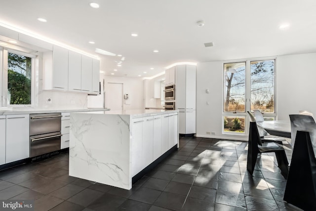 kitchen with white cabinets, a center island, light stone countertops, and tasteful backsplash