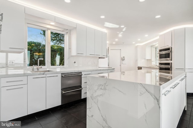 kitchen with white cabinets, a kitchen island, light stone counters, and sink