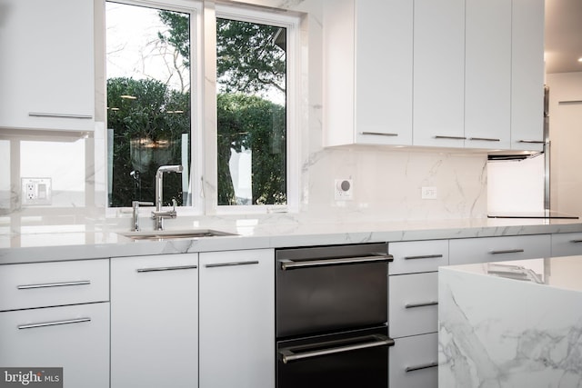 kitchen with light stone countertops, white cabinetry, and sink