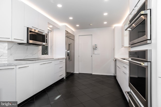 kitchen with light stone countertops, backsplash, white cabinets, dark tile patterned flooring, and appliances with stainless steel finishes