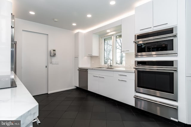 kitchen with appliances with stainless steel finishes, white cabinetry, dark tile patterned flooring, and sink