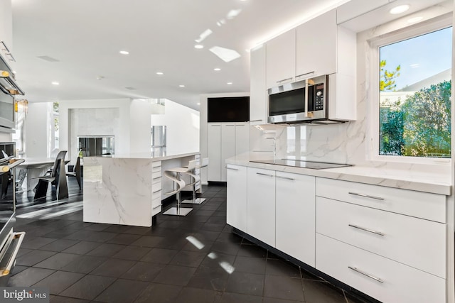 kitchen featuring decorative backsplash, black electric cooktop, a center island, white cabinetry, and plenty of natural light