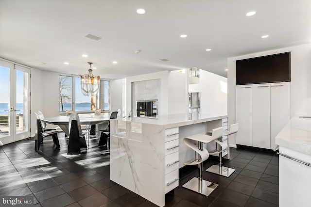 kitchen featuring pendant lighting, a water view, white cabinetry, and dark tile patterned floors