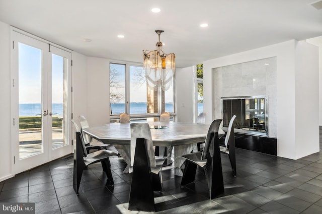 dining area with a fireplace, french doors, a water view, and a notable chandelier