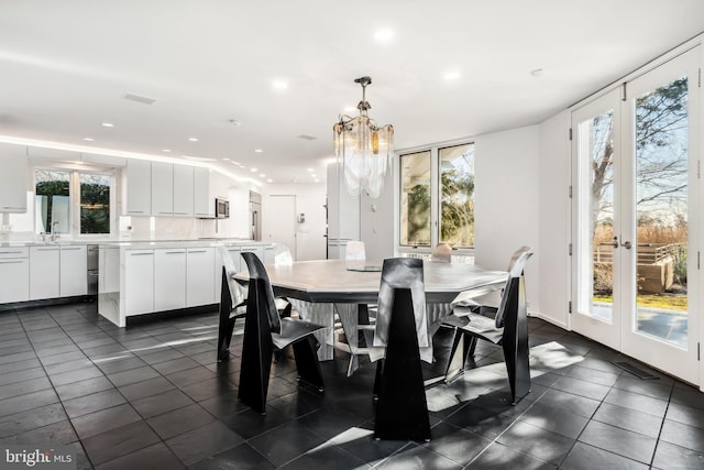 tiled dining space featuring sink, plenty of natural light, french doors, and a notable chandelier