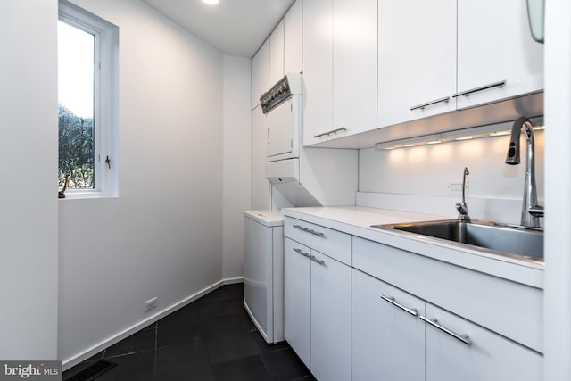 kitchen with white cabinets, stacked washing maching and dryer, dark tile patterned flooring, and sink