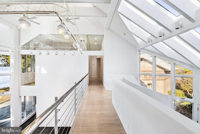 hallway with beam ceiling, light hardwood / wood-style flooring, high vaulted ceiling, and a skylight